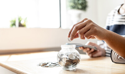 A woman is putting coins in a jar with a lot of coins inside, she is managing to divide her money to save money and invest it to make it grow even more. Concept of saving money and investing.