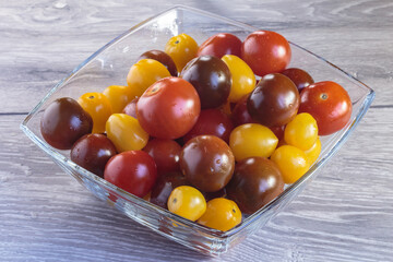 Multicolored tomatoes of different varieties in a glass bowl. Fashionable vegan food.