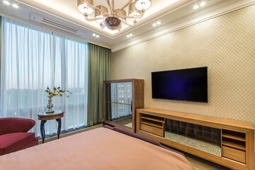 Modern comfortable, nicely decorated, elegant luxury master bedroom. A TV above the wooden cabinet and a wooden wardrobe. Interior design.
