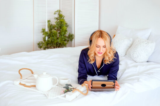freelancer works in pajamas on the bed with a cup of coffee behind on tablet. Online work from home. Homeschooling from home. online shopping from home