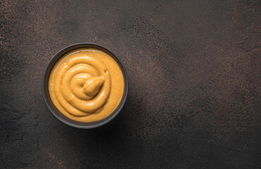 Mustard in a ceramic black cup on a brown background.