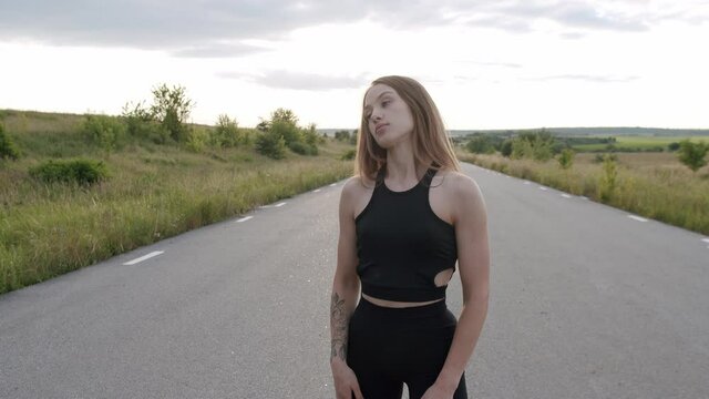 Long-haired, athletic girl having workout on the road among summer nature
