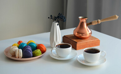 Two cup of coffee, multicolored macaroons, turkish coffee pot on white background, top view