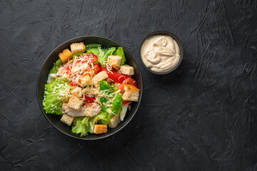 Fresh delicious salad with chicken breast, vegetables and lettuce leaves with sauce on a black background.