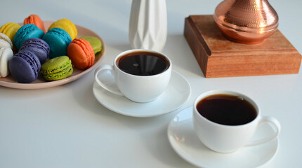 Two cup of coffee, multicolored macaroons, turkish coffee pot on white background, top view