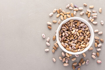 Fototapeta na wymiar Legumes in bowl and scattered in the background, Pinto beans in a plate on a gray background, top view, copy space