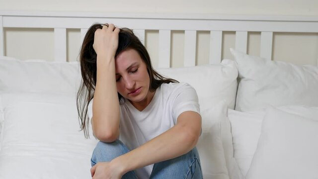 Tense young woman who looks down and thinks about personal problems. An upset girl feels lonely at home, suffers from depression, headache, worries about the wrong decision.