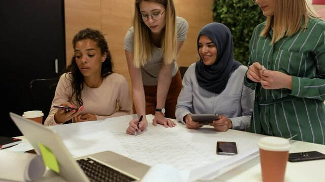 Group of multiracial women working together on architectural designs in the creative office.