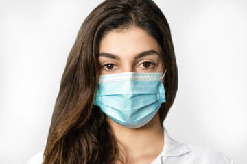 The beautiful face of a young girl with surgical mask on neutral background.