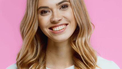 happy young woman smiling while looking at camera isolated on pink