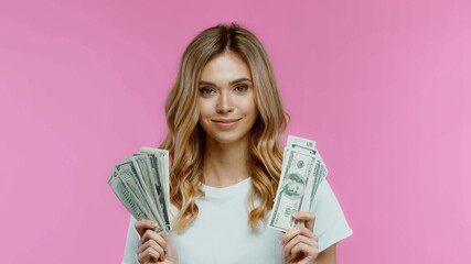 Cheerful young woman in white t-shirt holding dollars isolated on pink