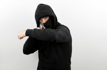 Criminal man wearing balaclava and hoodie holding pistol, standing shooting with a gun