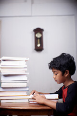 Little schoolboy study hard with stack of books at home