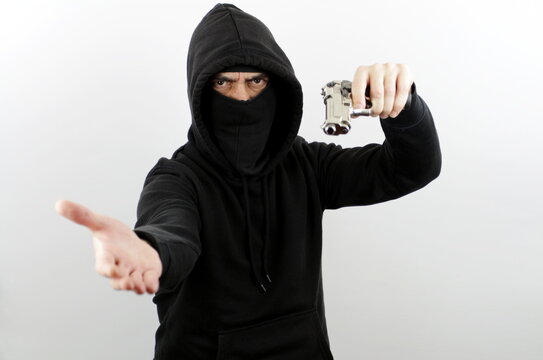 Criminal man wearing balaclava and hoodie pointing a gun while asking for money. Crime concept
