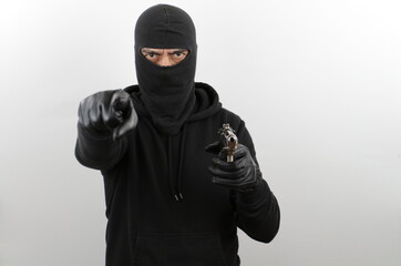 Man wearing black balaclava holding pistol, pointing finger at the cameraover isolated white...