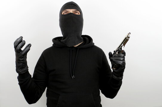 Criminal man wearing balaclava holding pistol, standing with angry expression