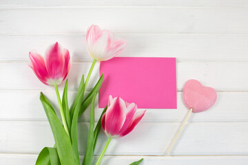 Fototapeta premium Colorful tulips and candy in the shape of a heart on white wooden background.