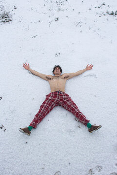 Joven alegre tumbado sobre la nieve desnudo