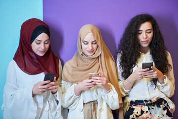 Muslim women using mobile phones isolated on blue and purple background