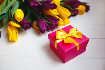 pink gift box with yellow bow on the background of a bouquet of tulips