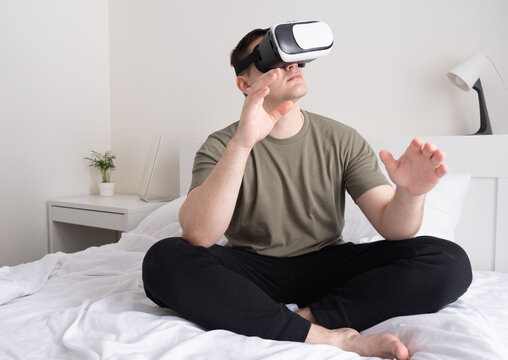 Man wearing virtual reality glasses. The guy sits on the bed and looks in the vr helmet