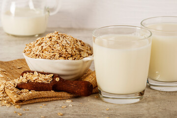 Oatmeal in a white bowl with a glass of milk on a white blue background. A healthy, nutritious morning breakfast. Oat milk. Healthy vegan non-dairy organic drink with flakes. 