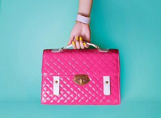 Woman hand with yellow manicured nails holding pink purse on blue background.  - 419694390