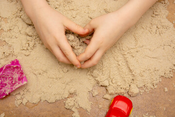 small Child plays with kinetic sand and toys. Sensory experiences of the child, happy childhood.