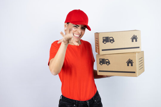 Young beautiful woman wearing courier uniform holding delivery packages smiling funny doing claw gesture as cat, aggressive and sexy expression