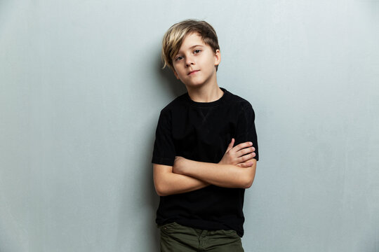 A 9-year-old boy in a black T-shirt stands with crossed arms. Grey background. Space for text.