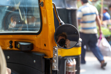 Passenger of a tuktuk or bajai during a ride in the busy streets of Mumbai taking a selfie picture with a professional DSLR camera in the rear view mirror.