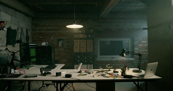 Empty Loft Office of Electronics Startup at Night. Nobody in Bare Brick Garage made as Modern Business Workplace for IT workers. Workspace with Computer, Bike, Lamp, Shelves and Supplies. 4K Pan Shot