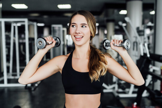 Portrait of an attractive sports girl with dumbbells in her hands, time for sports, workout, modern gym