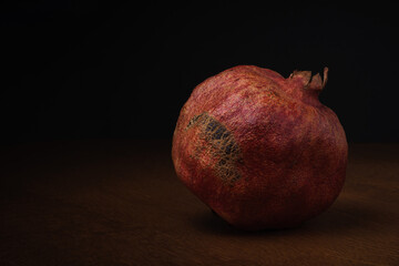 ripe red dried pomegranate on a wooden table on a black background. minimalistic moody still life...
