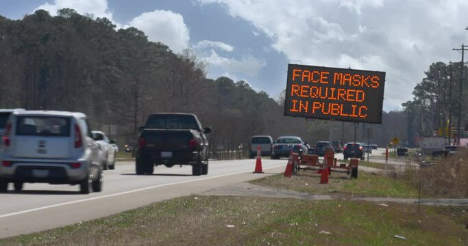 A temporary road construction lighted sign next to a highway warns traffic of the dangers of COVID-19. Text is customizable upon request.	