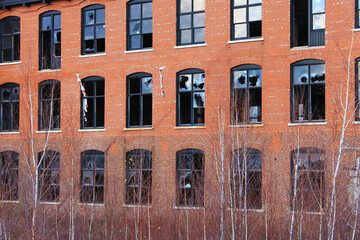 Obraz premium An old, abandoned, brick building that is falling into ruin, with broken windows and overgrown yard.