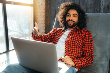 Stylish african american man in a red plaid shirt working at a laptop and looking at the camera