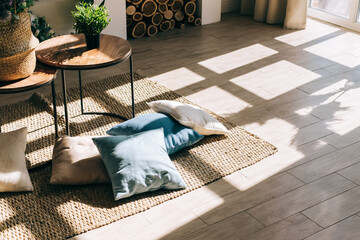 Interior of bright living room in scandinavian style with coffee table and pillows on the floor, big shadow from window on the floor. © nikkimeel