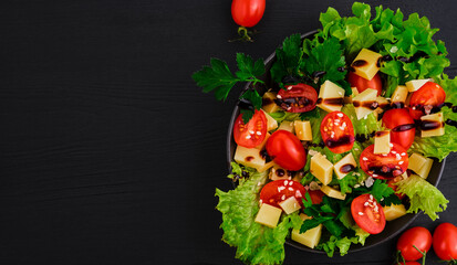 Tomato salad with lettuce, goat cheese, fresh vegetables with sesame seeds and olive oil on a black wooden table. Top view with copy space. Healthy vegetarian food, banner