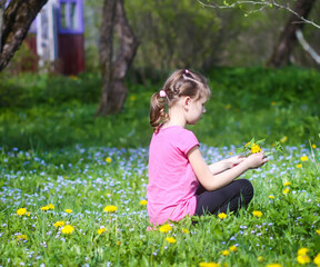 A girl on the green spring meadow with a lot of wildflowers in sunlight. Child exploring nature.