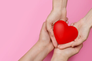 two people holding a heart in their hands on a pink background copy space. the concept of support, charity and helping people