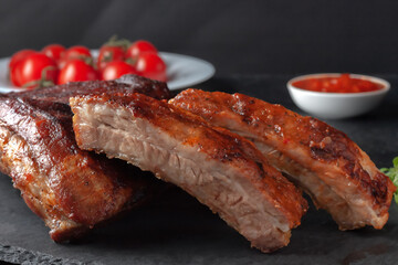 Grilled pork ribs, served on a graphite board with tomatoes