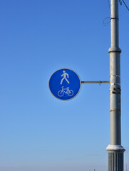 there is a bicycle and pedestrian road sign hanging on the street post, winter sunny day. blue sky background