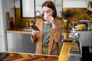 Young woman in a hurry to work in the morning, wearing jacket, drinking coffee and chatting on...