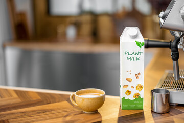 Packaging of vegetable milk near a cup of coffee, pincher and coffee machine on wooden table top on the kitchen. Organic nut dairy, alternative drink. Copy space.
