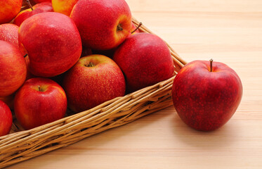 One apple and a group of red apples in a basket on the table.