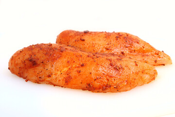 Raw chicken breast coasted in a dry rub of Cajun spices on a white background. Could be used as a food prep image or the dangers of raw chicken.