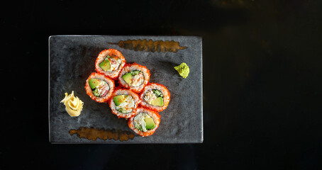 California sushi roll with crab, avocado, cucumber and tobiko caviar served on a plate with wasabi and ginger. Isolation on a black background. Japanese food