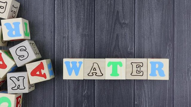Colourful wooden toy alphabet blocks spelling word - Water over a dark grey plank background with copyspace. Stop motion, top view
