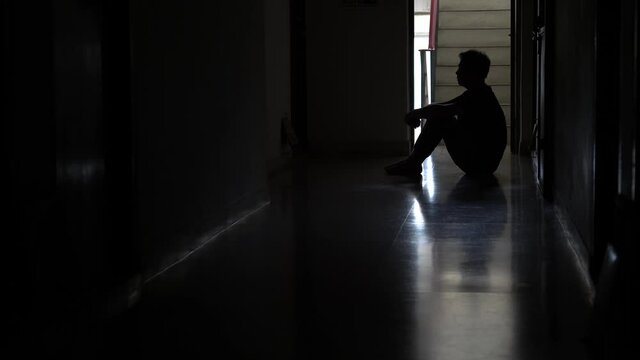 Silhouette of a stressed man sitting in the dark leaning against the wall, Stress, violence, The concept of depression and suicide.
